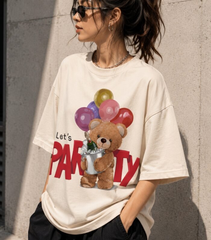 Woman wearing LURI Let's Party Bear graphic oversized t-shirt front full view – teddy bear with balloons and champagne on cream Supima cotton